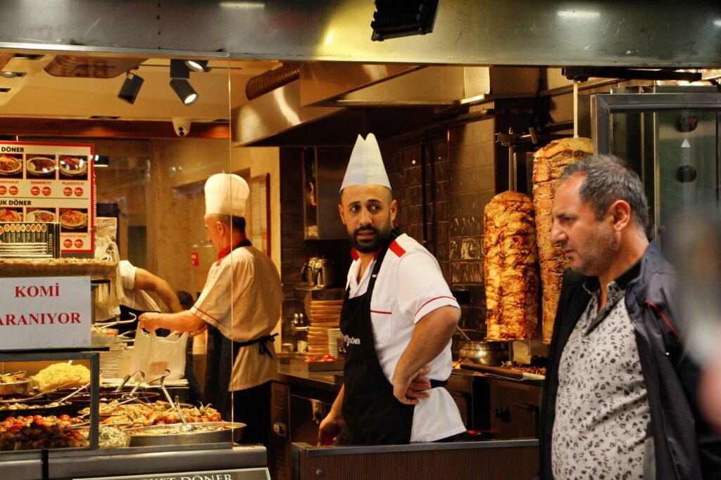 A vibrant scene inside a Turkish döner kebab shop with chefs and a patron.